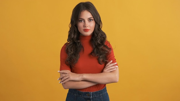 Beautiful brunette girl in red top with hands crossed confidently looking in camera over colorful background