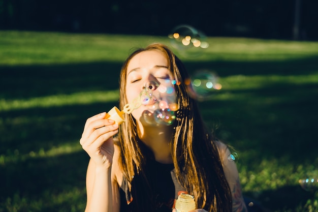 Free Photo beautiful brunette girl with long hair puffs up soap bubbles in the park