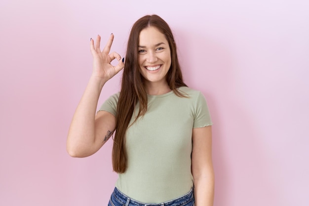 Free photo beautiful brunette woman standing over pink background smiling positive doing ok sign with hand and fingers successful expression