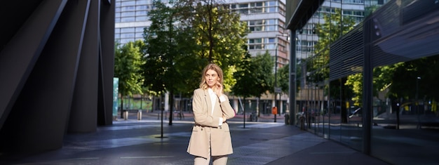 Free Photo beautiful businesswoman in beige suit standing near office buildings on street posing with confident