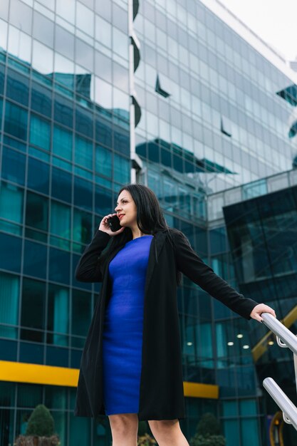 Beautiful businesswoman talking on smartphone in front of building