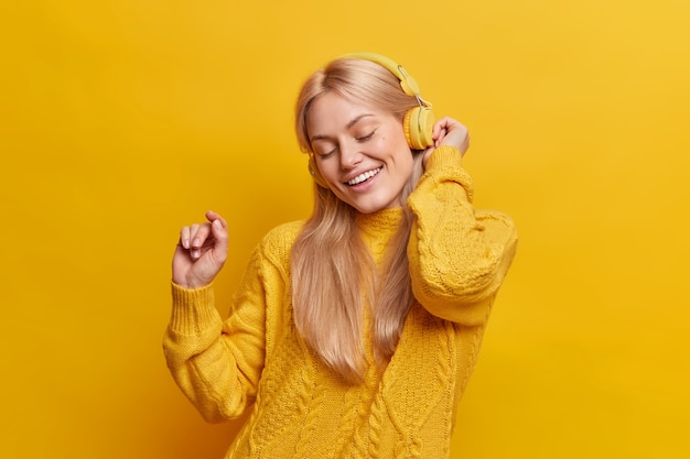 Free Photo beautiful carefree blonde woman dances keeps arm raised relaxes with pleasant music from headphones