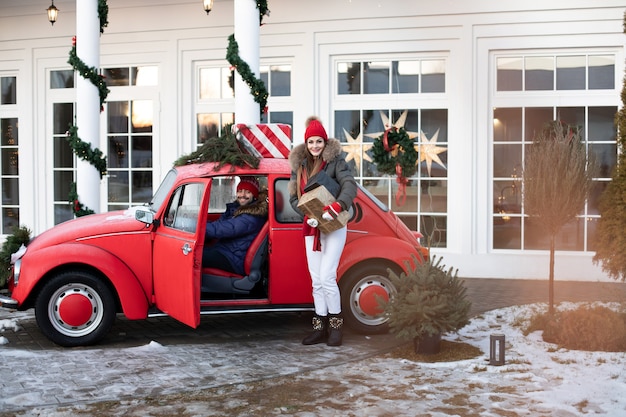 Beautiful Caucasian girl in warm winter clothes carries boxes with Christmas gifts in a red car to her husband