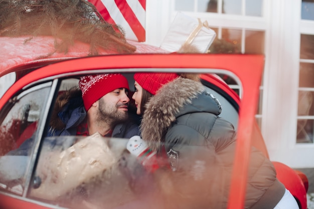 Beautiful Caucasian girl in warm winter clothes carries boxes with Christmas gifts in a red car to her husband