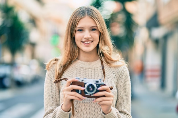 Beautiful caucasian teenager smiling happy using vintage camera at the city.