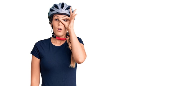 Beautiful caucasian woman wearing bike helmet doing ok gesture shocked with surprised face, eye looking through fingers. unbelieving expression.