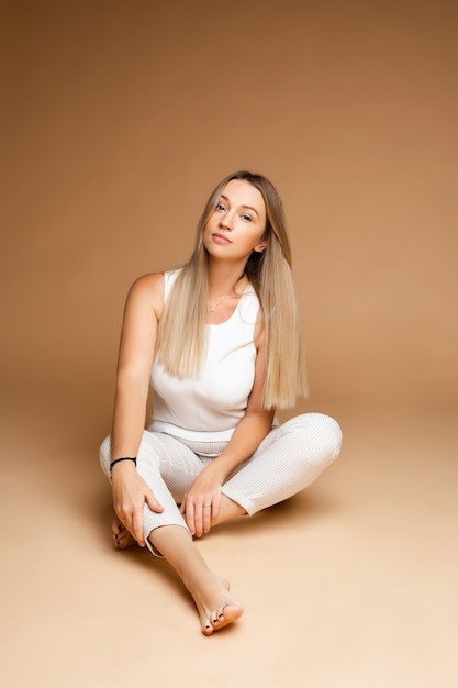 Beautiful caucasian woman with fair hair sits on the floor, picture isolated on brown background