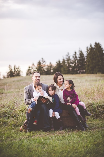 Beautiful cheerful family with a mother, father and three kids reading the Bible in the park