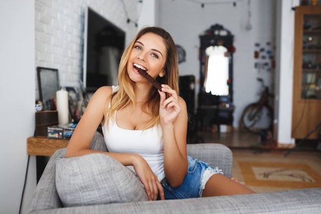 Beautiful cheerful young woman eating bite of chocolate