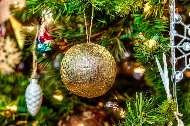 Beautiful closeup of a golden ball and other decorations on a Christmas tree with lights