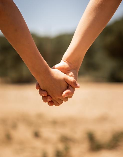 Free photo beautiful closeup shot of a couple holding hands on a blurred background of a field