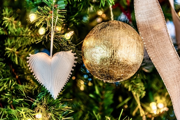 Beautiful closeup of a white heart-shaped ornament and golden ball on a Christmas tree