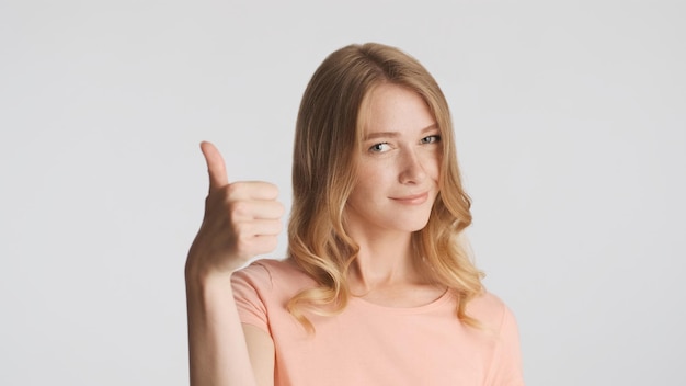 Free Photo beautiful confident blond girl keeping thumb up on camera isolated over white background body language concept