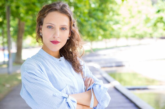 Beautiful confident girl with arms folded posing in park