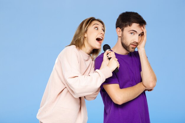 Beautiful couple over blue wall. Girl singing in microphone man didpleased.