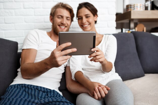 Beautiful couple looking at tablet smiling sitting on sofa  home.