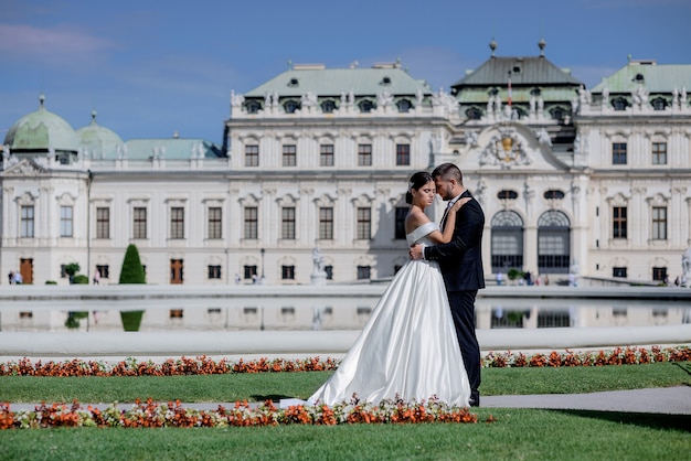 Beautiful couple in love dressed in the wedding attires in front of palace on the beautiful sunny day, wedding trip