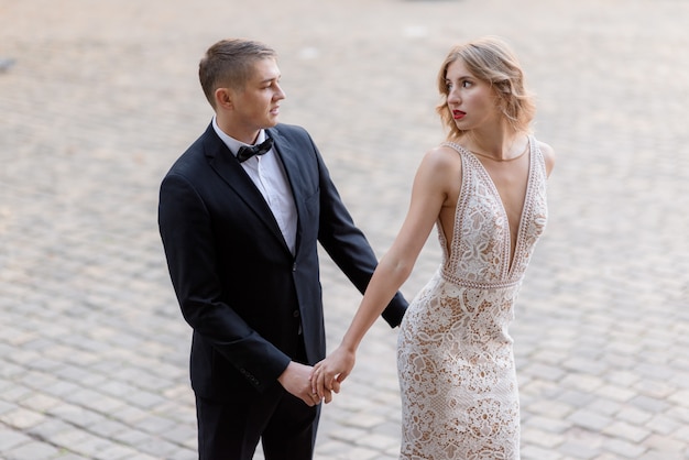 Beautiful couple in love in elegant attires is passionately looking on each other and holding together hands outdoors