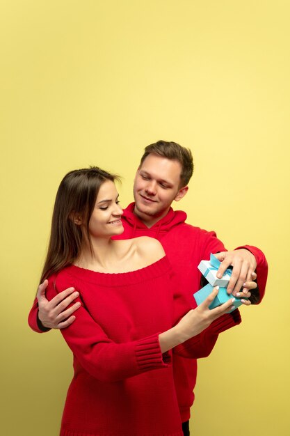 Beautiful couple in love opening gift on yellow studio wall