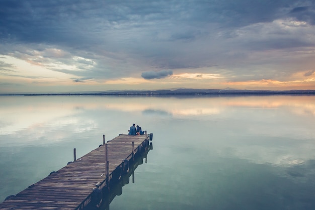 Beautiful couple sitting on a wooden dock under a beautiful sunset sky