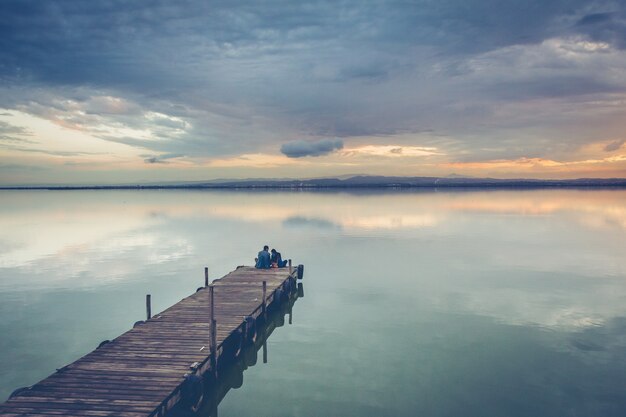 Beautiful couple sitting on a wooden dock under a beautiful sunset sky