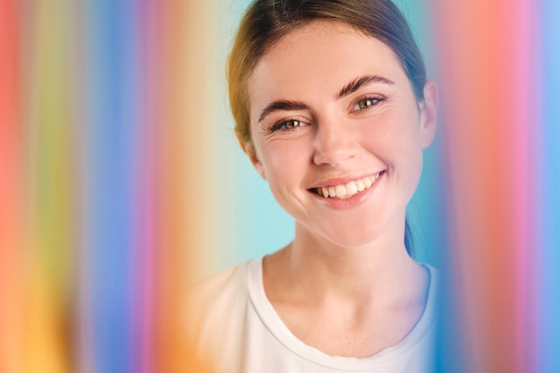 Beautiful cute girl joyfully looking in camera through rainbow over colorful background isolated