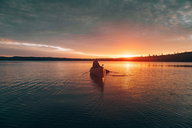 Free photo beautiful distant shot of a woman riding  kayak in the middle of a lake during sunset