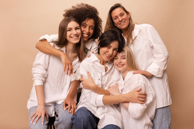 Beautiful diverse young ladies in jeans and white shirts look at camera on beige background Women's day concept