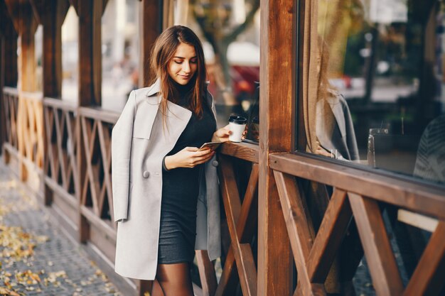 beautiful elegant girl standing in the autumn city and drinking a coffee