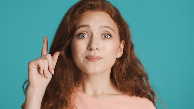 Beautiful excited redhead girl holding finger up having new idea over colorful background