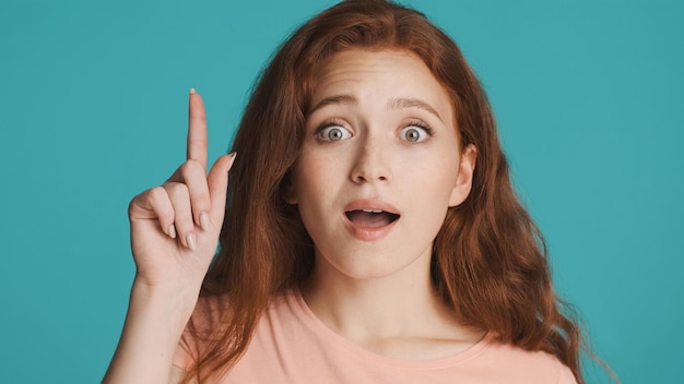 Beautiful excited redhead girl showing new idea gesture amazedly looking in camera over colorful background Wow expression