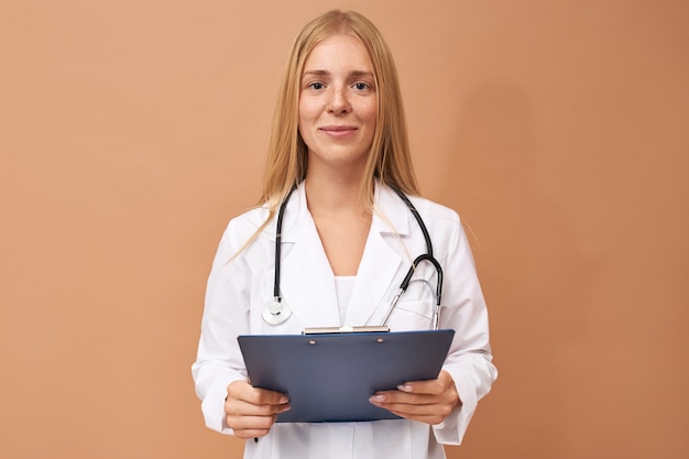 Free photo beautiful experienced young female practitioner in white surgical coat holding clipboard