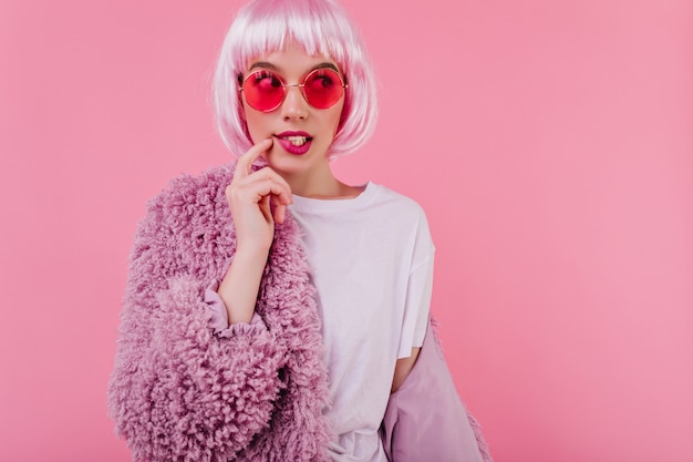 Free Photo beautiful fashionbale girl in sunglasses posing on pink wall in fur jacket. jocund stylish lady in periwig having fun at photoshoot