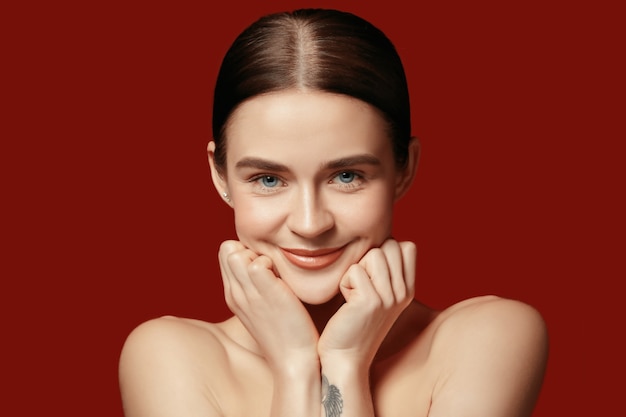 Free photo a beautiful female face. perfect and clean skin of young caucasian woman on red studio.