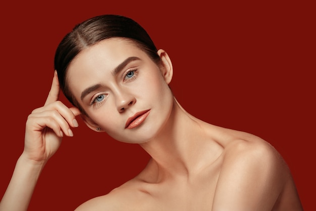 Free photo a beautiful female face. perfect and clean skin of young caucasian woman on red studio.