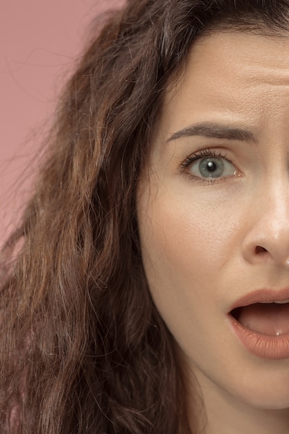 Free photo beautiful female half face portrait isolated on trendy pink studio background. young emotional frustrated and bewildered woman. human emotions, facial expression concept.