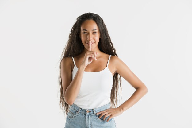 Beautiful female half-length portrait isolated on white wall. Young emotional african-american woman with long hair. Facial expression, human emotions concept. Whispering a secret.