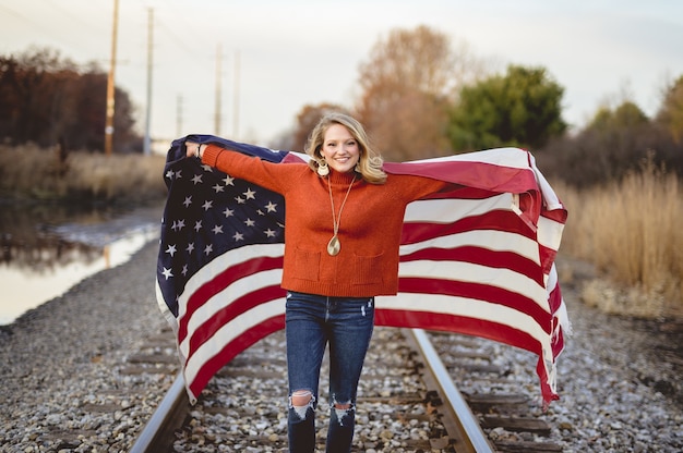 Free photo beautiful female holding the american flag while standing on railway