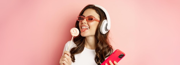 Free Photo beautiful female model listening music in headphones holding lolipop and mobile phone posing in sung