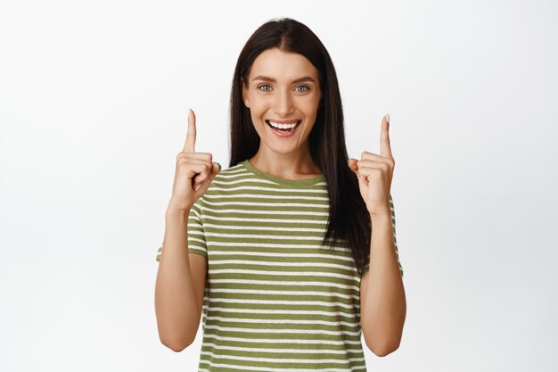 Beautiful female model smiles points fingers up shows sale logo banner stands against white background