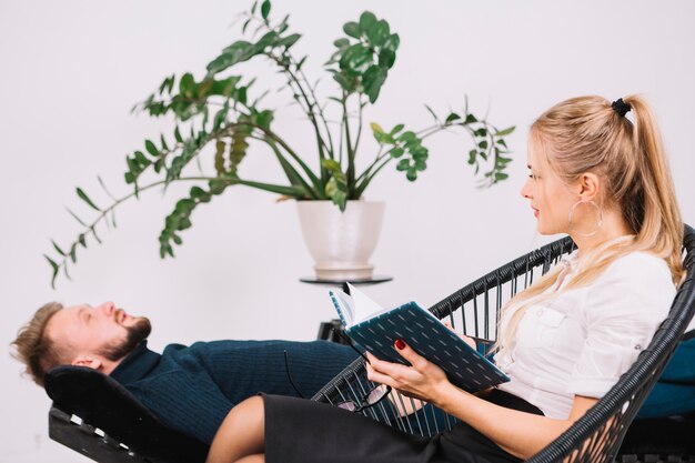 Beautiful female psychologist looking at male patient lying on couch in the clinic