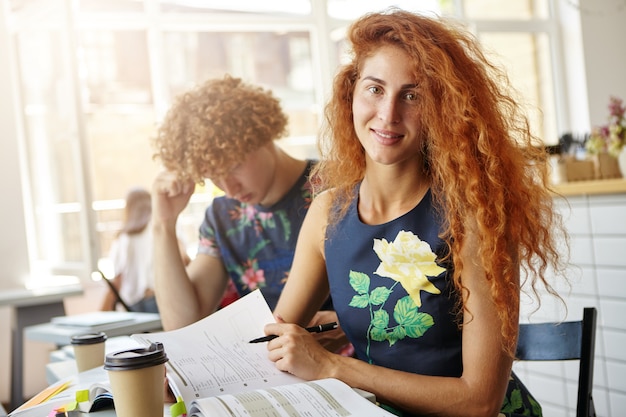 Free photo beautiful female sitting at coffe shop making exercises in her copybook