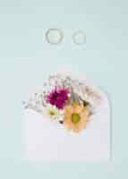 Free photo beautiful flowers inside the white envelope with two wedding rings on blue background