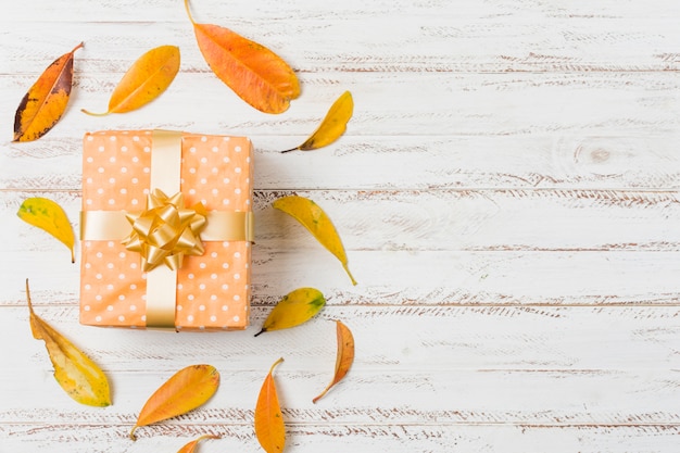 Beautiful gift box and autumn leaves over table with space of text