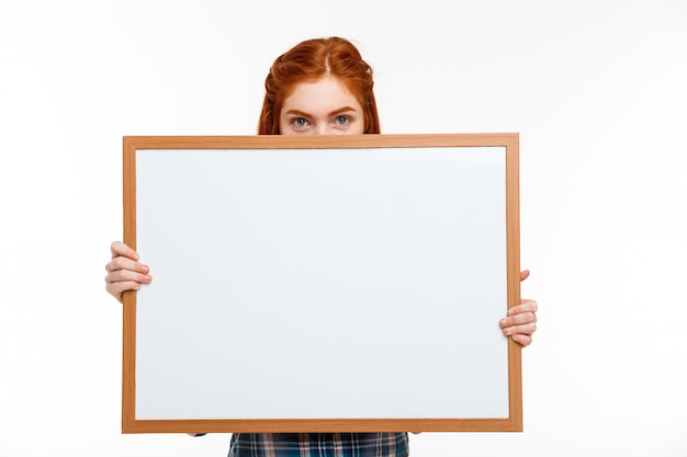 Free photo beautiful ginger girl with whiteboard over white wall.