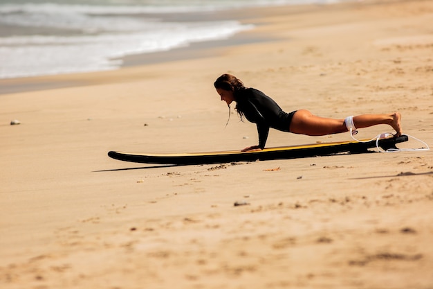 Beautiful girl get up on a surfboard on the sand.