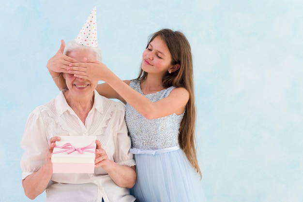 Beautiful girl giving surprised gift by covering her grandmother's eyes