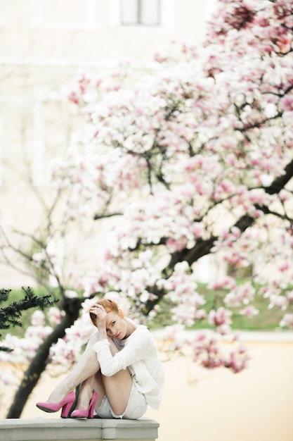 Free Photo beautiful girl is sitting at the railing near the amazing magnolia tree