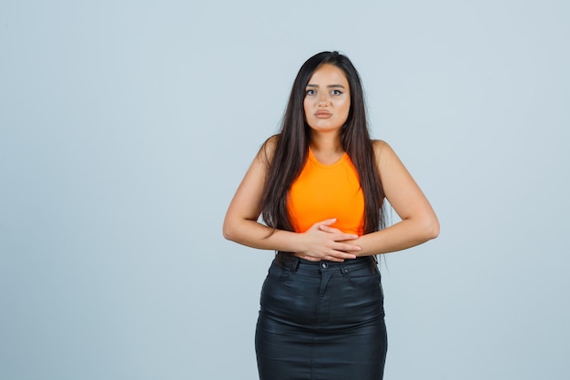 Free photo beautiful girl keeping hands on stomach in orange top and skirt and looking painful , front view.