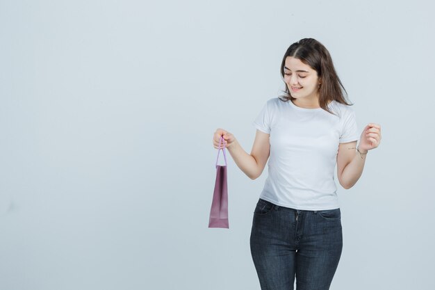 Beautiful girl keeping papper bag in t-shirt, jeans and looking happy , front view.